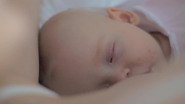 A close up of a baby girl's sleepy face. A six months old baby is almost sleeping while a mother is breastfeeding her
