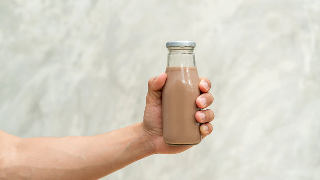 Men holding a bottle of chocolate milk on gray background.
