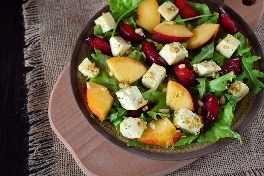 Fruit salad with arugula, plums, nectarines and soft cheese on a plate