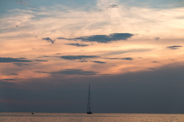 A sailing boat sails along the Croatian coast at sunset.