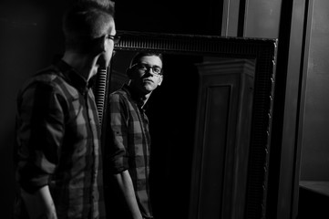 The guy looks in the mirror. Young handsome guy in the plaid shirt. Guy in the interior.