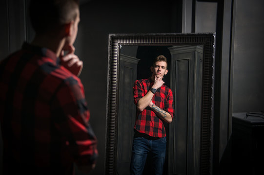 The guy looks in the mirror. Young handsome guy in the plaid shirt. Guy in the interior.