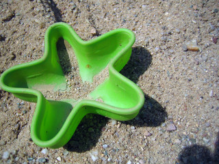 Green plastic sand toy shaped like a starfish lying in the sand