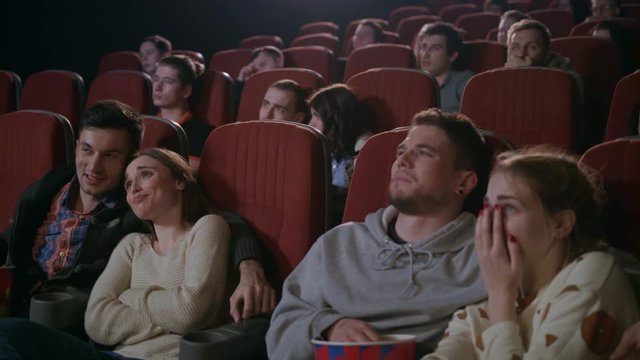 Young people watching movie in cinema. Love couples embracing and watching exciting movie. Romantic date at cinema. Enamoured couples looking melodrama. Cinema love concept