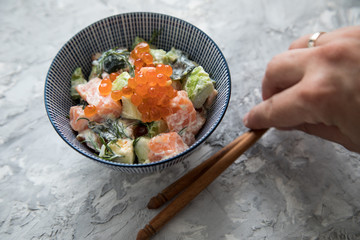 Frau serviert rohes Lachs Avocado Tatar mit Keta Kaviar und Holz Stäbchen