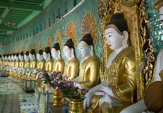 Meditating buddha statues with golden rope along the green wall