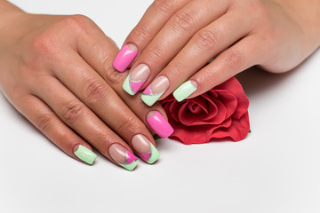 Obraz na płótnie Canvas summer mint pink manicure with silver stripes on long square tanned hands with a red rose in hands 
