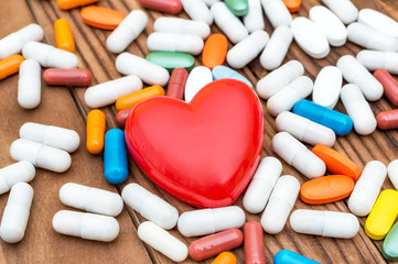 Red heart with pills on wooden background. Medical background.
