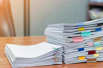 Stack of student's homework that assigned to students to be completed outside class on teacher's desk separated by colored paper clips. Document stacks arranged by various colored paper clips on desk.