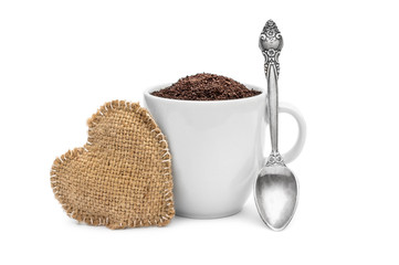 Full cup of ground coffee with spoon and heart of burlap on white.