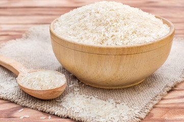 Wooden bowl and wooden spoon with rice on burlap napkin.