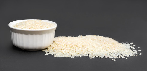 Ceramic bowl of rice with pile of rice on black.