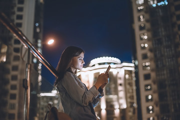 side view of attractive woman using smartphone on street with night city lights on background