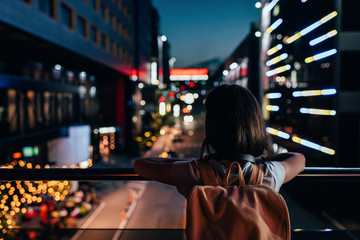 rear view of woman with backpack standing on street and looking at night city lights