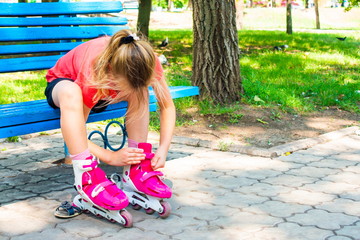A blond girl dresses red rollers, sitting in a park on a blue bench.