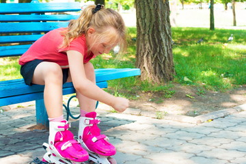 A blond girl dresses red rollers, sitting in a park on a blue bench.