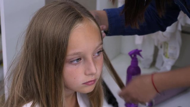 Hairdresser combing blonde hair and making hairstyle for child