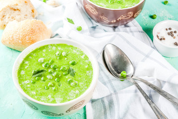 Green pea soup with fresh bread on light blue concrete table, copy space