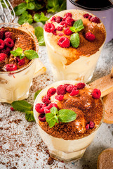Three portioned glass with Italian dessert Tiramisu, with mint and raspberries, on grey stone background.  Copy space