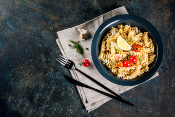 Classic italian pasta fusilli with pesto sauce, tomatoes, lime and fresh herbs in dark bowl, dark blue background  copy space top view