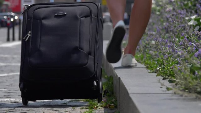A woman with a suitcase walks along a curb - closeup from the ground