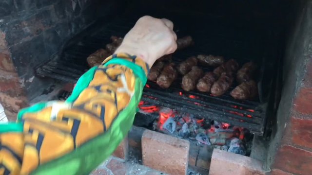 Woman preparing traditional Romanian dish of grilled ground meat rolls, called mititei, on barbecue in outdoors.