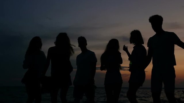 After sunset time. End of party. Silhouttes group of friens dancing on the beach near the campfire.