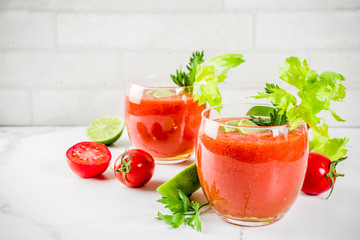 Summer veggie food, Cold soup gazpacho in glasses with with fresh celery, parsley and lime juice. White marble background copy space