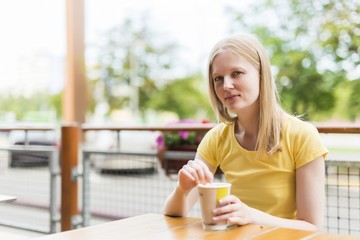 girl in casual clothes sitting with a paper cup of coffee in a street cafe