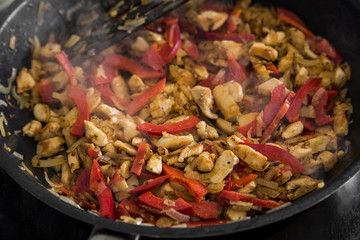 Chopped chicken, red Bulgarian pepper and onions are fried in a frying pan, closeup