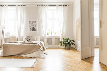 Spacious and bright bedroom interior with beige decorations, hardwood floor and a book on the...