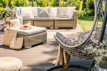 Pillows on rattan couch near table on patio with hanging chair in the garden. Real photo