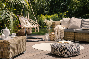 Pouf on wooden terrace with rattan sofa and table in the garden with hanging chair. Real photo