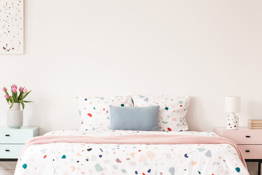 Real photo of a double bed with dotted sheets and pillows on an empty wall between nightstands in a bedroom interior. Place for your painting/poster/clock © Photographee.eu