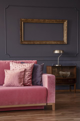 Pink sofa next to wooden cabinet with gold lamp in living room interior with mockup. Real photo