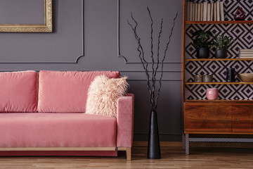 Pink sofa next to black decor and wooden cabinet in vintage living room interior. Real photo