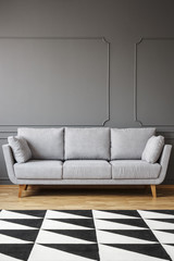 Black and white carpet in front of grey sofa in minimal living room interior with copy space. Real photo