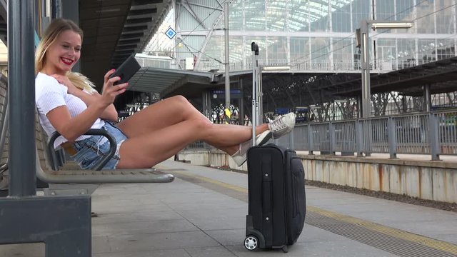 A young beautiful woman takes selfies on a train station platform