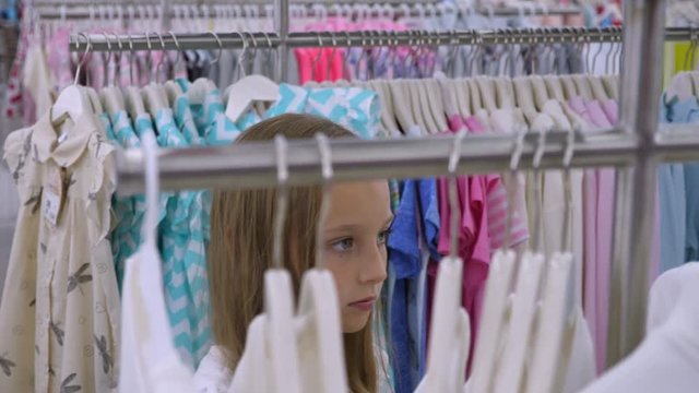 Young blonde girl choosing fashionable clothes in boutique