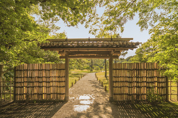 Small outdoor bamboo gate of the garden of Rikugien under the maple trees that let in the rays of the sun.