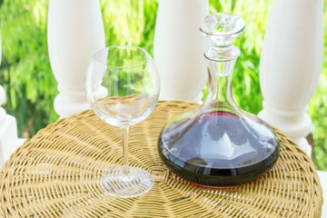 Empty Glass Decanter with Red Wine on Rattan Wicker Table in Garden Terrace of Villa or Mansion. Authentic Lifestyle Image. Relaxation Indulgence Gourmet. Poster with Copy Space
