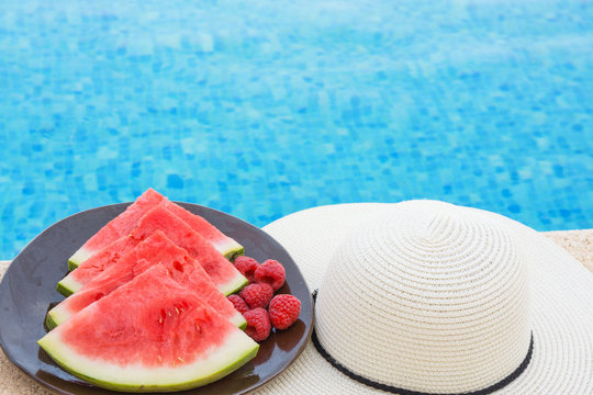 Wedges of Ripe Juicy Seedless Watermelon Raspberries on Plate on Rattan Table by Swimming Pool. Vacation Relaxation Summer Vibes. Authentic Atmosphere. Lifestyle. Poster Banner