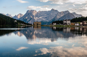 Fototapeta na wymiar Buildings along the shoreline are reflected in the calm waters of Lake Misurina in the Italian Dolomites, just before sunset.