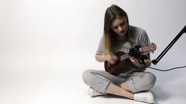 A singer with a little guitar ukulele. Girl with guitar okulele sings sitting on white background.