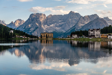 Buildings along the shoreline are reflected in the calm waters of Lake Misurina in the Italian Dolomites, just before sunset.