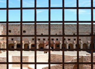 View of the fortress courtyard through the bars of the window of a prison cell
