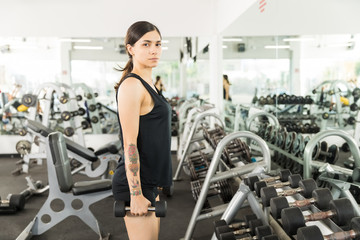 Fototapeta na wymiar Woman With Dumbbells Standing In Front Of Mirror At Gym