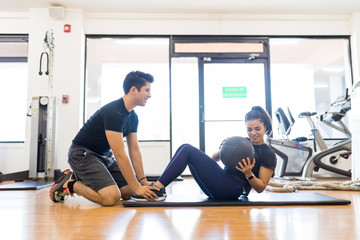 Instructor Assisting Woman In Doing Abdominal Exercise With Medicine Ball