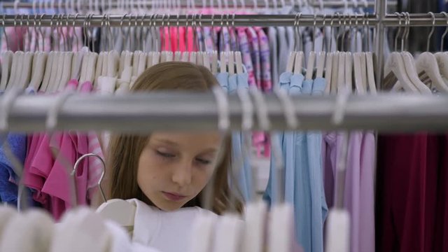 Blonde girl fitting clothes on hangers and shopping in boutique
