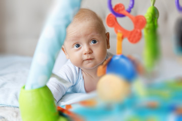 Charming baby in blue body, lies on the tummy and looks at the developing mat
